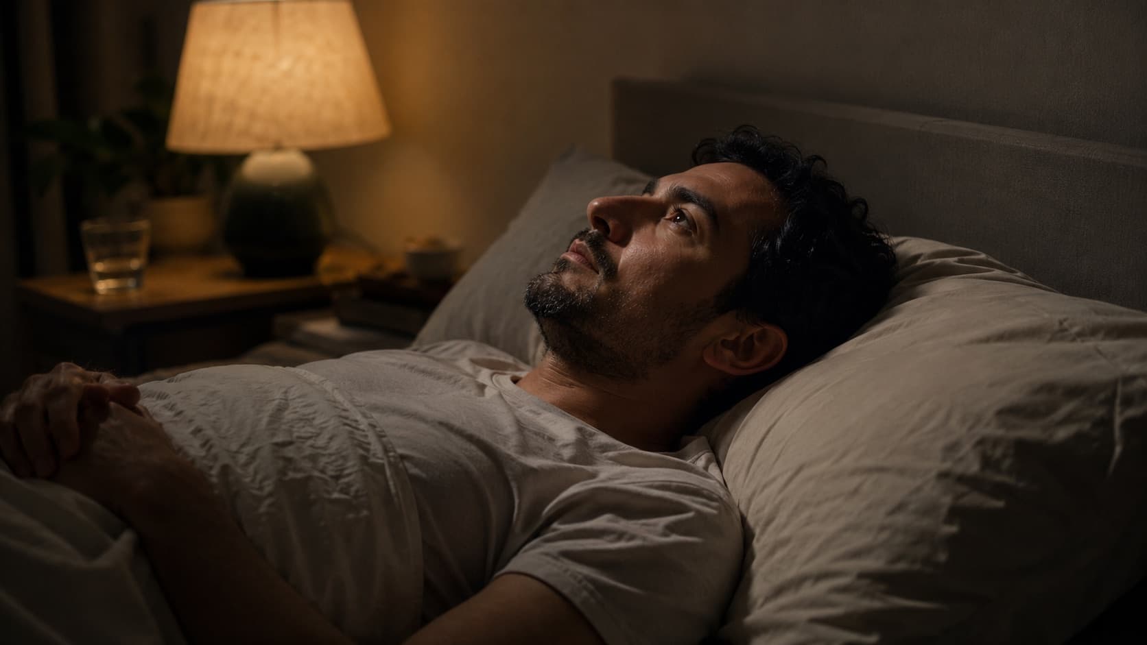 Un uomo sveglio a letto di notte guarda il soffitto, illuminato da una lampada calda